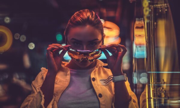 Attractive pensive styilish woman is posing for photographer in neon lights. There are darkness at background. Beautiful pensive trendy girl is posing for photographer in neon lights. There are darkness at background.